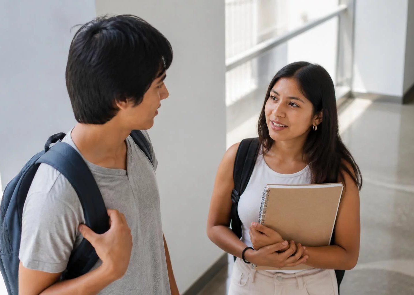 Dos estudiantes con mochila conversando en un pasillo universitario